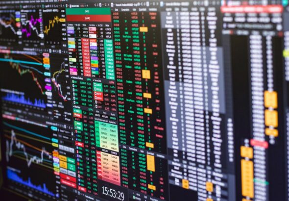 Trader analyzing candlestick charts and risk parameters on multiple trading screens